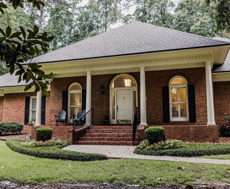 A front side view of an updated red brick ranch traditional house home with off white columns and brick front steps with curb appeal.